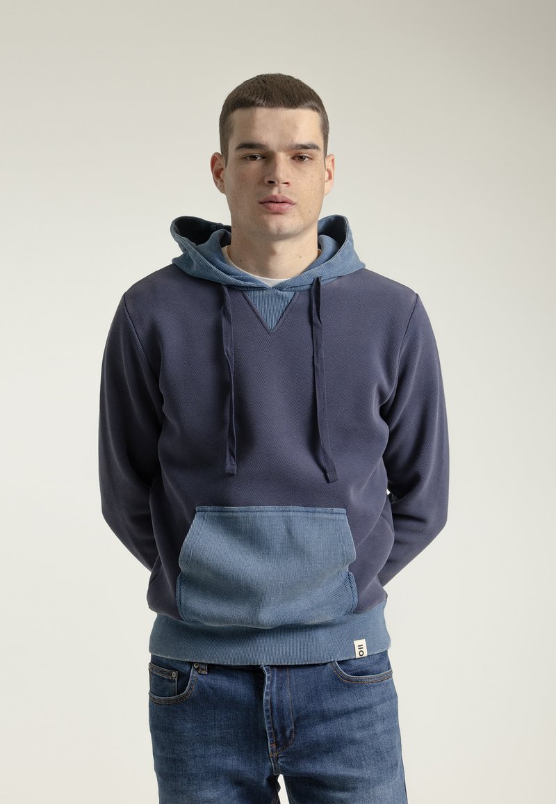 Sudadera de color azul marino con una capucha forrada en un tono de azul más claro y un bolsillo tipo parche. Fabricada con un tejido texturizado, cuenta con un diseño en V y cordones.