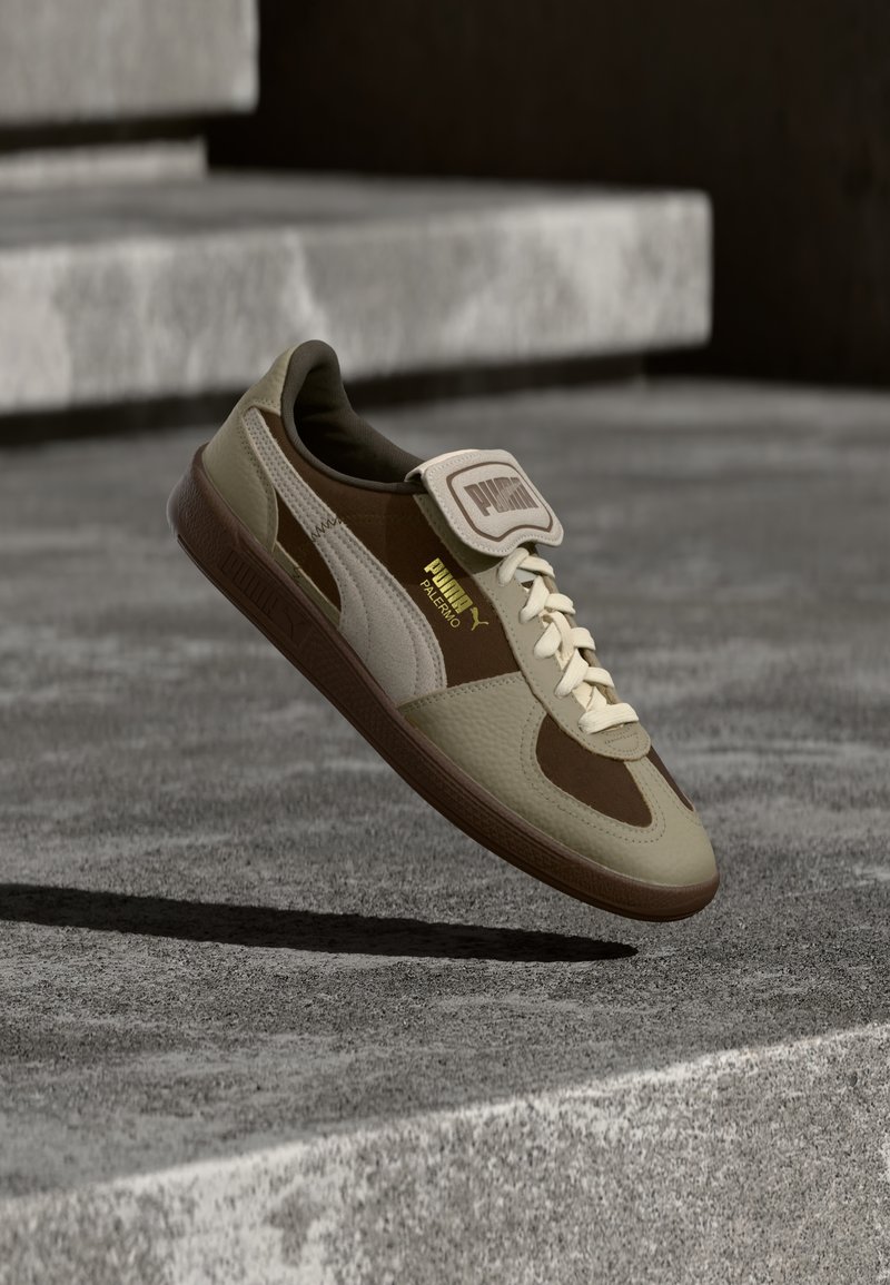 Sneaker, mis sisaldab kerget pruuni ja tan nahka ning siidist materjale, padjaga keel ja klassikaline nöörkinnitus. Kuldsed logo aktsendid.