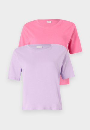 Roze T-shirt met korte mouwen gecombineerd met lichtblauwe denimshorts. Accessoires zijn een kleine witte handtas en witte hoge sneakers.