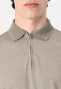 Le polo gris présente un col texturé avec un zip quart. Le tissu a un tissage subtil, offrant un design décontracté et respirant.