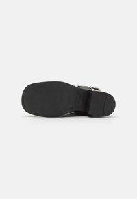 Suela de zapato negra con textura suave y forma redondeada. Presenta un ligero tacón y un área de marca. Sin patrones o acentos visibles.