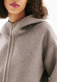 Haut de hoodie en mélange de laine gris avec un col montant, doté d'une fermeture éclair dorée. Texture douce, coupe décontractée et éléments de design simples.