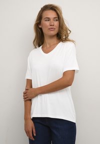 T-shirt en coton blanc avec un col en V et des manches courtes, doté d'une coupe décontractée et d'une texture douce. Associé à un jean bleu foncé.