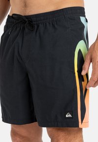 Schwarze Schwimmshorts mit elastischem Bund, Kordelzug und einem lebhaften Farbverlauf in Orange, Gelb und Grün an der Seite.