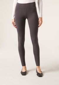 Leggings taille haute, gris foncé, en tissu doux et extensible. Design ajusté sans coutures visibles, associés à des chaussures noires.