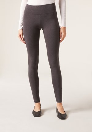Högmidjade, mörkgrå leggings i ett mjukt, stretchigt material. Åtsittande design utan synliga sömmar, tillsammans med svarta skor.