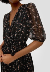 Svart blommig klänning med genomskinliga puffärmar, med en v-ringning och en åtsittande midja, prydd med små rosa och blå blomstertryck.