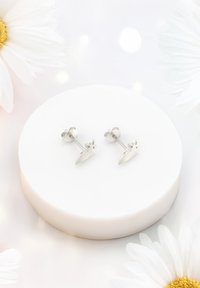 Orecchini a stud in argento a forma di coniglietto, con superfici lucide e dettagli intagliati, esposti su un pedestal circolare bianco e liscio.