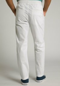 Witte katoenen broek met een elastische tailleband, voorzien van twee achterzakken, gecombineerd met blauwe canvas sneakers.
