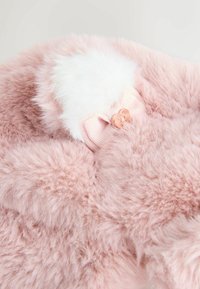 Mäkký ružový umelý kožušinový materiál s nadýchaným bielym akcentom a svetloružovou stuhou v podobe mašle. Obsahuje dva dekoratívne ružovozlaté gombíky na mašli.