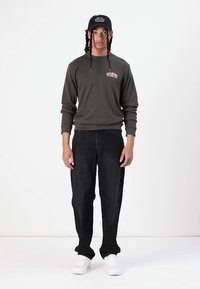 Dark gray sweatshirt with a small, light design on the chest, paired with loose black jeans and white sneakers. Black cap on head.