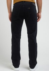 Mörkblå kordflodbyxor med rak passform; framträdande bakfickor och subtil textur; kombinerat med vita sneakers.