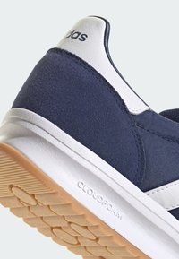 Marinblå sneakers med vita accenter, som har en texturerad ovandel, vadderad krage och en gummisula med ett mönstrat däck. "CLOUDFOAM" präglat på sulan.