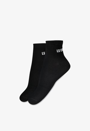 Calcetines de algodón negros hasta el tobillo con textura acanalada y la marca blanca "LE COQ" en el puño. Forma de puntera estándar con costuras reforzadas.