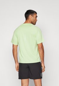 Light green short-sleeved athletic shirt with a reflective accent, paired with black shorts, displayed from a rear angle.