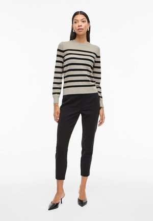 Pull rayé beige et noir, fabriqué en matériau doux, associé à un pantalon noir sur mesure et des escarpins noirs à bout pointu.