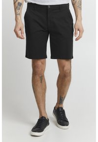 Black cotton shorts with a straight-leg design, a single button closure, and hemmed cuffs. Worn with black sneakers.