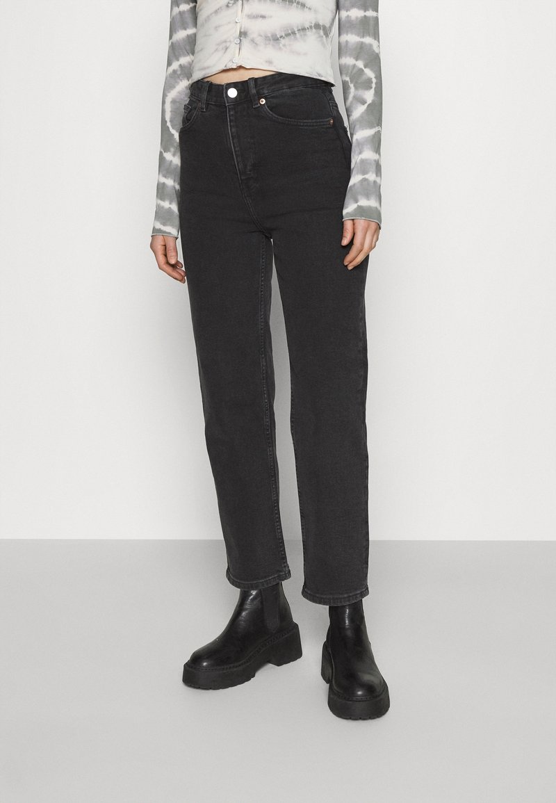 Jean noir taille haute à coupe droite avec des détails de couture. Associé à un haut à manches longues tie-dye et des bottes noires épaisses.
