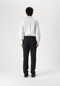Men's black trousers with a straight leg, made of durable fabric. Features two back pockets and is paired with a white striped shirt.