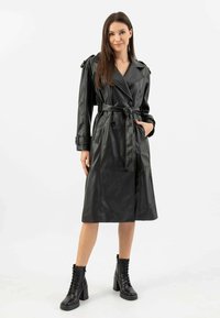 Cappotto trench in pelle nera con vita regolabile da cintura, parte anteriore doppiopetto, tasche con patta e lunghezza fino ai polpacci, impreziosito da spalline.