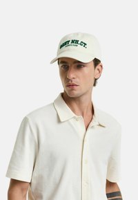 Weißer Baumwollhut mit grünem Text "GANT NH. CT. SPORTS CLUB" auf der Vorderseite, mit einem gebogenen Schirm und einem klassischen Sechspaneldesign.