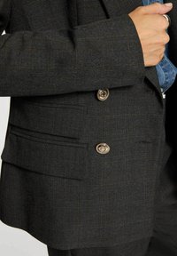 Blazer grigio scuro con motivo a quadri, texture del tessuto, dettagli con bottoni argentati e design a doppia tasca. Vestibilità sartoriale con spalle strutturate.