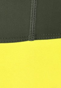 Mustaa ja keltaista kangasta, jossa on sauma erottuvalla ompeleella. Tekstuurin pinta näyttää sileältä, ja keltaisessa osassa on kirkas, matta pinta.