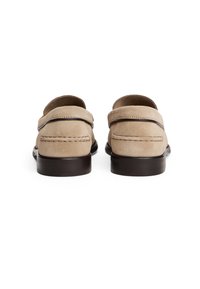 Beige mokkasiner i semsket skinn med brun flat såle, med et enkelt stikkedesign og detaljer med bakrem. Glatt tekstur med minimale accenter.
