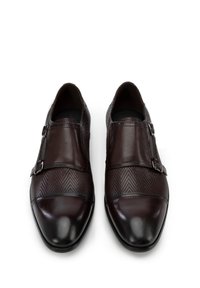 Zapatos de cuero marrón con un upper texturizado, que cuentan con una puntera lisa y dos hebillas ajustables en el lateral para un ajuste seguro.