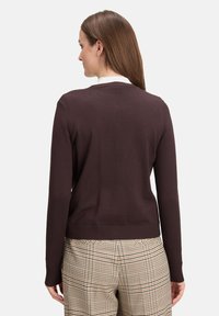 Dark brown sweater with a plain knit design and ribbed hem, paired with checkered beige and brown trousers. No visible fastenings or embellishments.