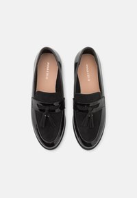 Μαύρα loafers φτιαγμένα από λείο και σουέτ υλικό, με επίπεδη σόλα, λεπτομέρεια με φουντίτσες και λογότυπο στη σόλα. Λείος υφασμάτινος χαρακτήρας.