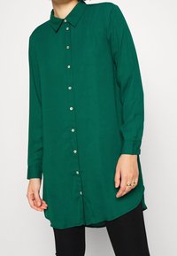 Groen overhemd met lange mouwen, knoopsluiting en kraag, met een gladde textuur en goudkleurige knopen, voorzien van een hoog-laag zoom.