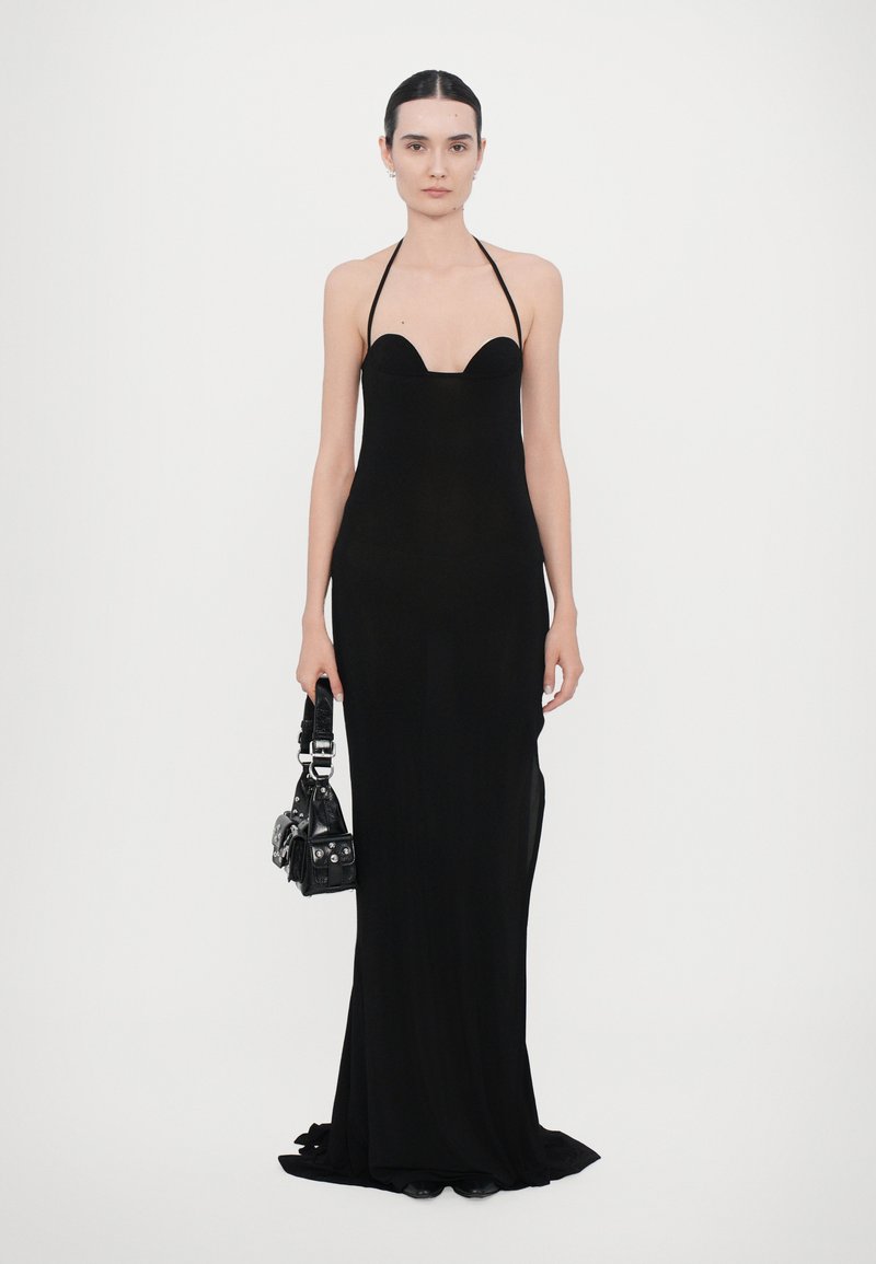 Black, fitted evening dress with a scoop neckline and halter straps, featuring a sleek, floor-length design. Accompanied by a small black bag.