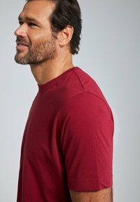 Bordeaux korteciloc shirt gemaakt van zachte katoen, met een ronde hals en zijnaaddetails, getoond vanuit een profielzicht.