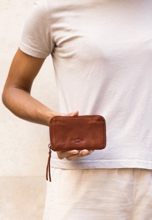 Hnedá kožená peňaženka so zipsom, s textúrovaným povrchom a malou strapcom. Logo je vyrazené na prednej strane.