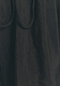 Svart texturerad tyg med en skrynklig yta och två rundade band. Materialet har en svag lyster som ger ett lager-på-lager utseende.