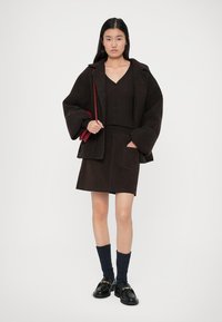 Brūns vilnas maisījuma pārmetnis, melns ribots topiņš, tumši brūns zamšādas mini svārki ar kabatu, tumši zils adīts zeķes un melni loafers.