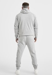 Gray hoodie and sweatpants set in soft, textured fabric. Hoodie with a drawstring and logo detail on the leg. Casual fit with ribbed cuffs.