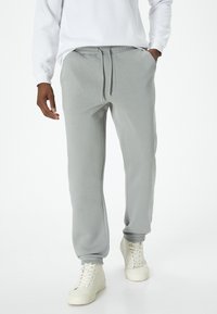Grijze sweatpants met een elastische tailleband en verstelbare trekkoord, voorzien van zijzakken en geribbelde boorden, gedragen met witte sneakers.