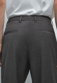 Pantaloni grigi con tessuto texture, vita elastica e due tasche posteriori. Design semplice, adatto per un abbigliamento casual o semi-formale.
