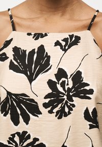 Μπλούζα αμάνικη σε μπεζ χρώμα με λεπτές μαύρες τιράντες, διακοσμημένη με μαύρο ανθικό σχέδιο και ευθεία λαιμόκοψη.