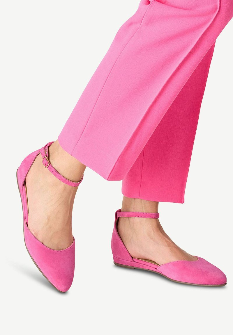 Chaussures plates en suede rose avec une bride de cheville, dotées d'un bout pointu et d'un petit talon, assorties à un pantalon rose.