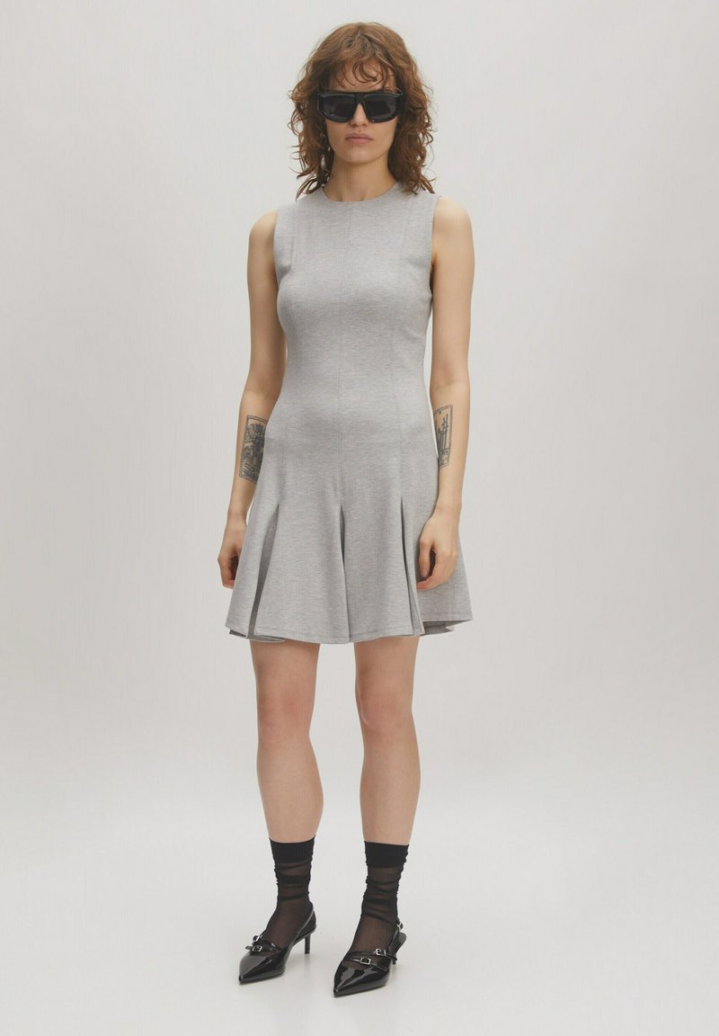 Graues ärmelloses Kleid mit taillierter Oberpartie und ausgestellt Rock, aus einem weichen Stoff gefertigt; kombiniert mit schwarzen spitz zulaufenden Absätzen und Sonnenbrille.