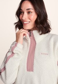 White fleece pullover with a half-zip front, featuring pink accents on the zipper and shoulders, soft texture, and embroidered logo detail.