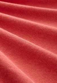 Tissu corail doux et texturé avec des plis délicats formant des lignes diagonales sur la surface.