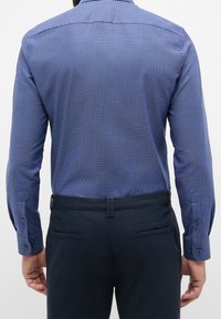 Niebieska, teksturowana koszula z długim rękawem i zapinanymi na guziki mankietami, zestawiona z ciemnymi spodniami z tylnymi kieszeniami i szlufkami na pasek.