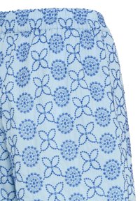 Tissu bleu clair avec ceinture élastique, présentant un motif répétitif de formes florales et circulaires brodées en bleu.