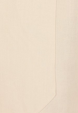 Close-up van beige stof met fijne textuur en een naad die verticaal loopt nabij de rechterrand, met gedetailleerd weefpatroon.