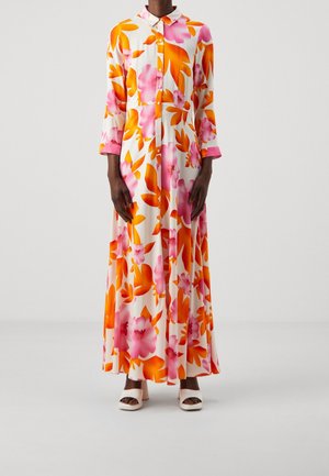 Valkopohjainen kukallinen maksimekko, jossa on suuret vaaleanpunaiset ja oranssit kukat, pitkät hihat, kaulus ja napillinen etuosa, yhdistetty valkoisiin sandaaleihin.