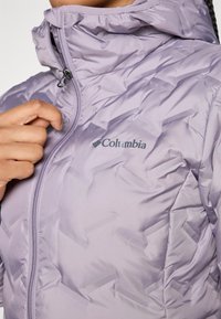 Doudoune lilas avec un col haut, dotée d'une fermeture éclair et du logo Columbia. Le tissu a un motif texturé et matelassé.